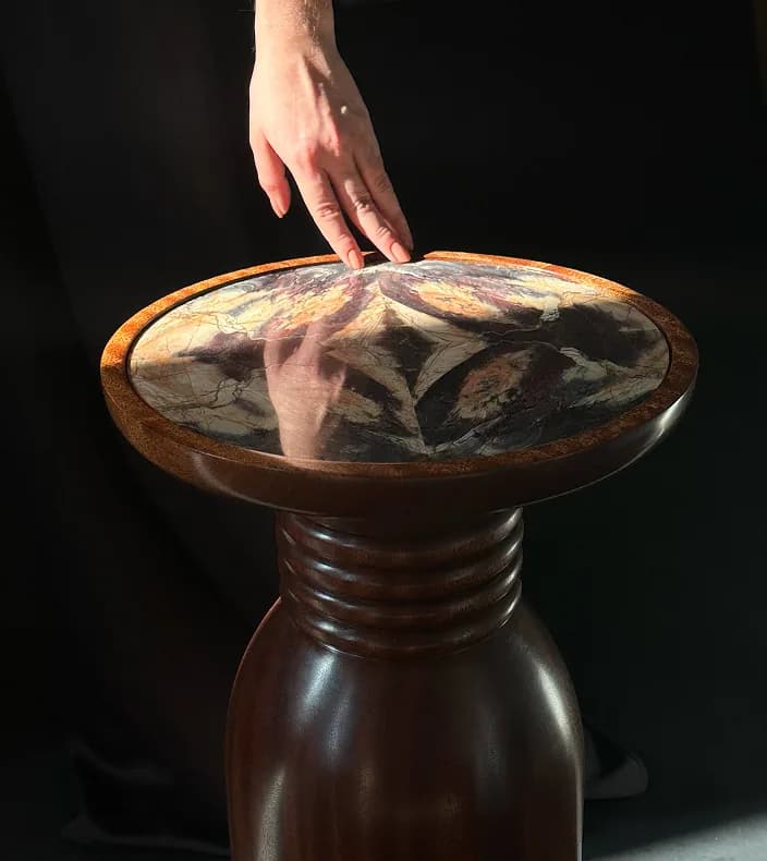 A hand resting on a jasper-topped pedestal table by Anna Kos.